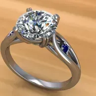 Silver ring with a large clear diamond and small blue side stones on a light wooden background
