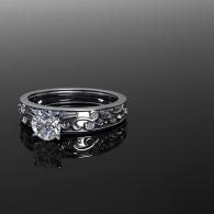 Black diamond ring with ornate band on reflective gray surface