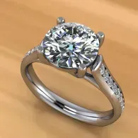 Silver ring with a large round diamond and smaller side stones on a warm tan background