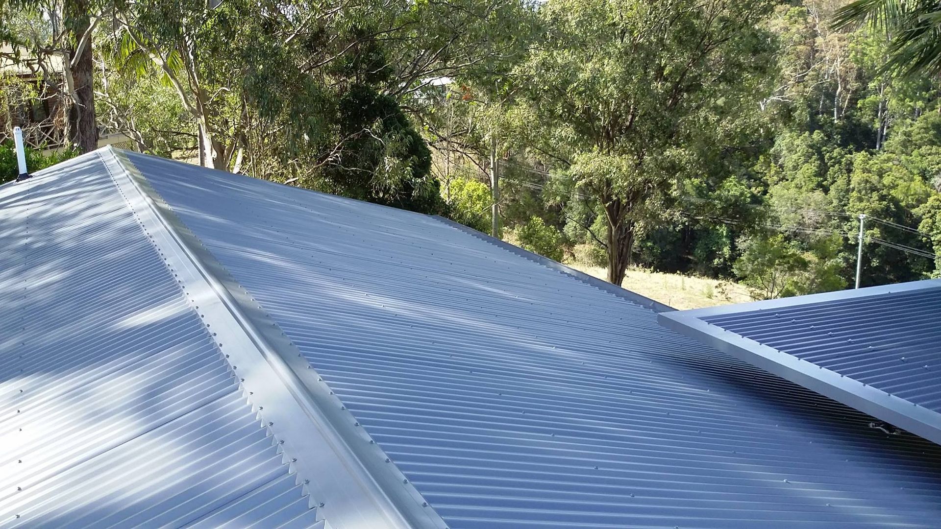 Gray Corrugated Metal Roof on a House, Trees in the Background, Sunny Day — Over the Top Roofing Specialists in Gympie, QLD