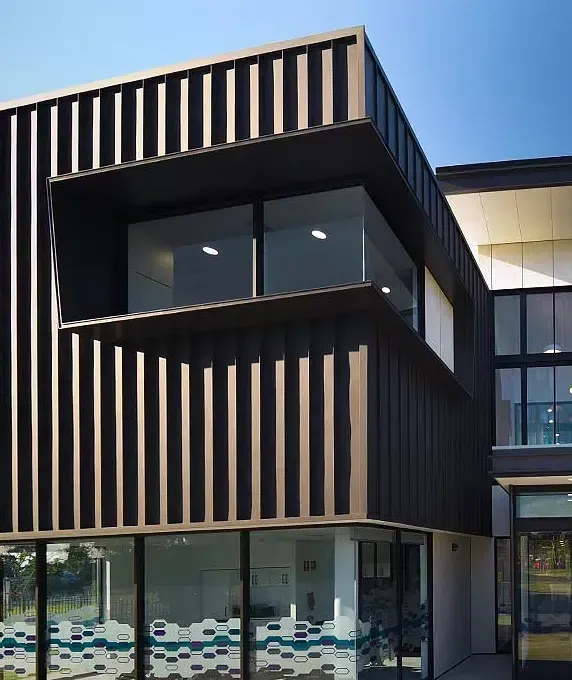 Modern Building With Dark Vertical Slats, Glass Windows, and a Blue Sky — Over the Top Roofing Specialists in Narangba, QLD