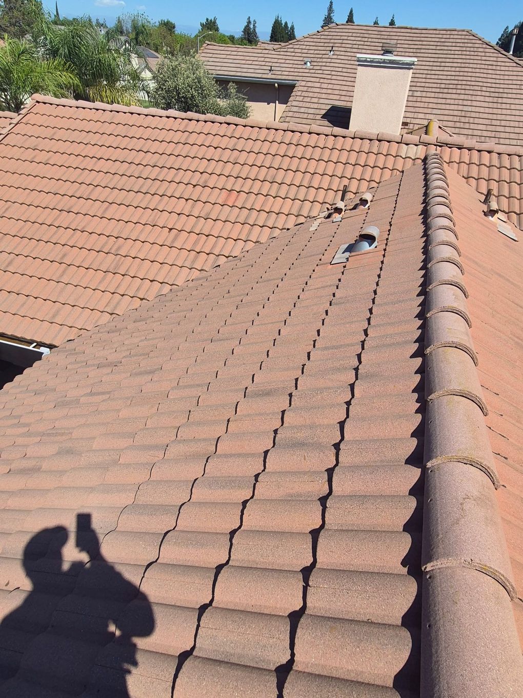 Two workers on a rooftop repairing red tiles under a bright blue sky
