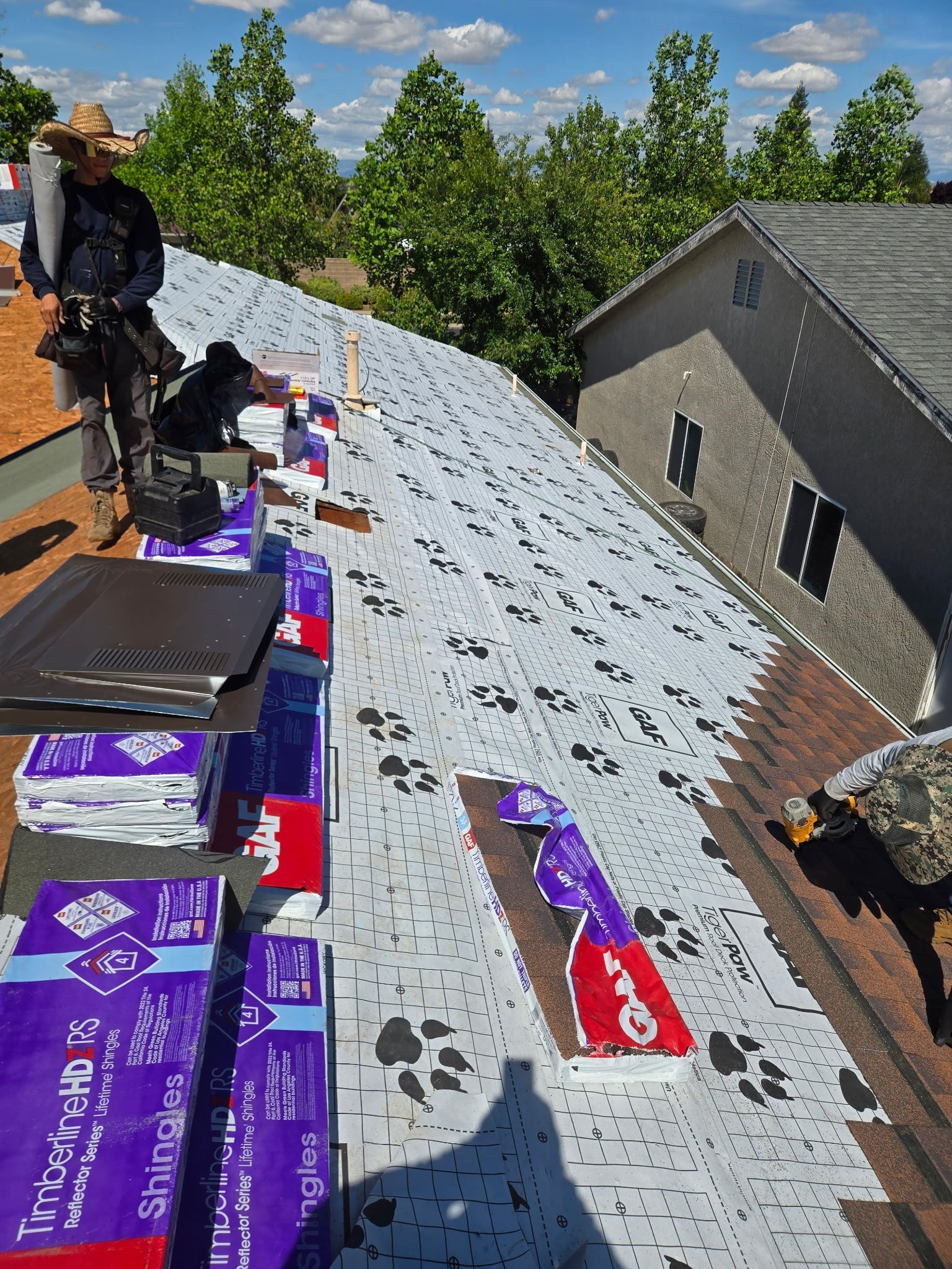 Sunlit rooftop covered in gravel with strings of small flags, utility poles, and neighboring houses in the distance
