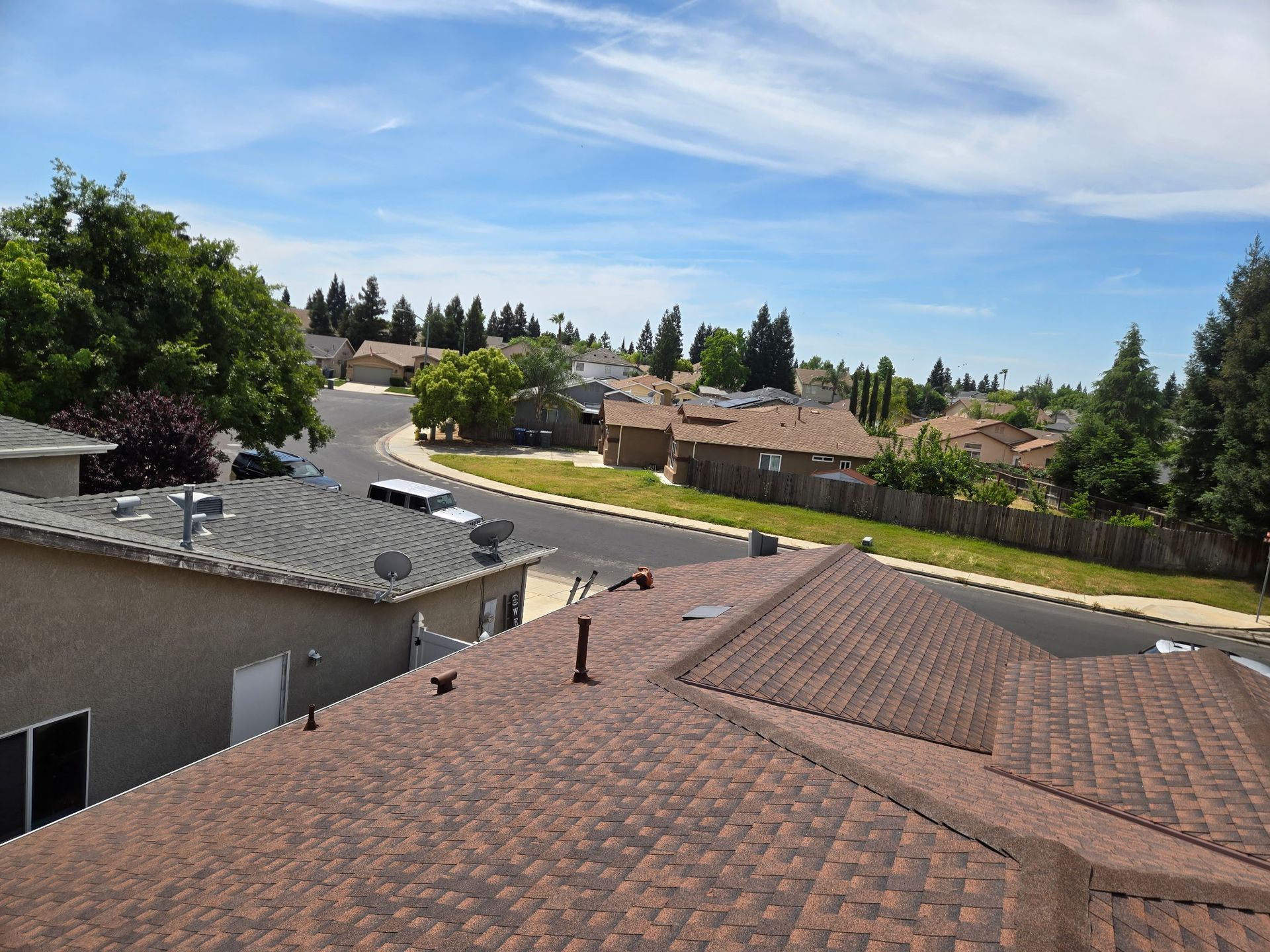 Gray shingled roof with vents and a chimney under a clear blue sky, seen from above