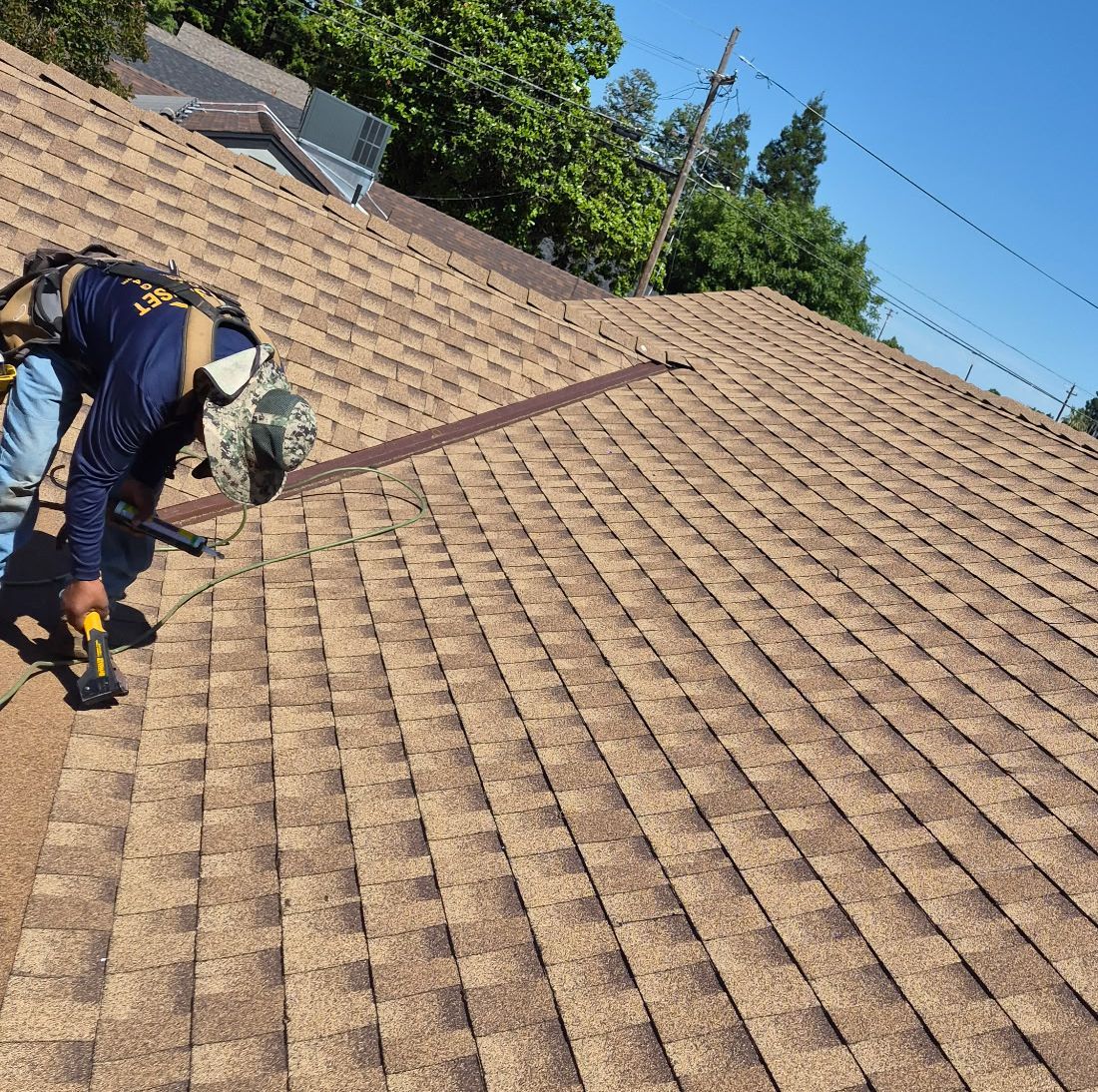 Worker installing shingles on a tan roof under a blue sky