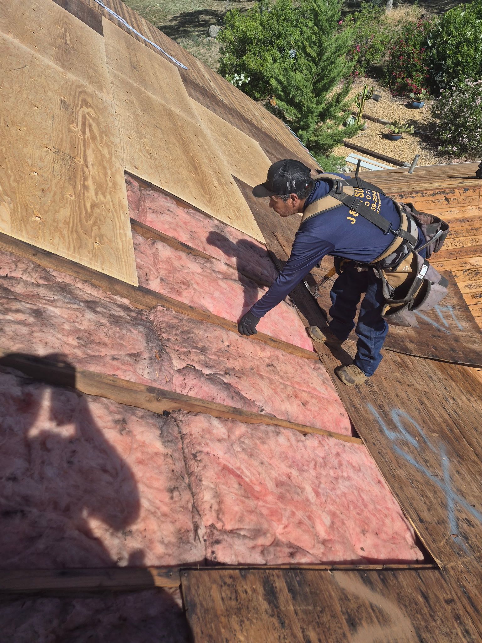 Worker in harness climbs a steep roof, applying material to a pink roof section.