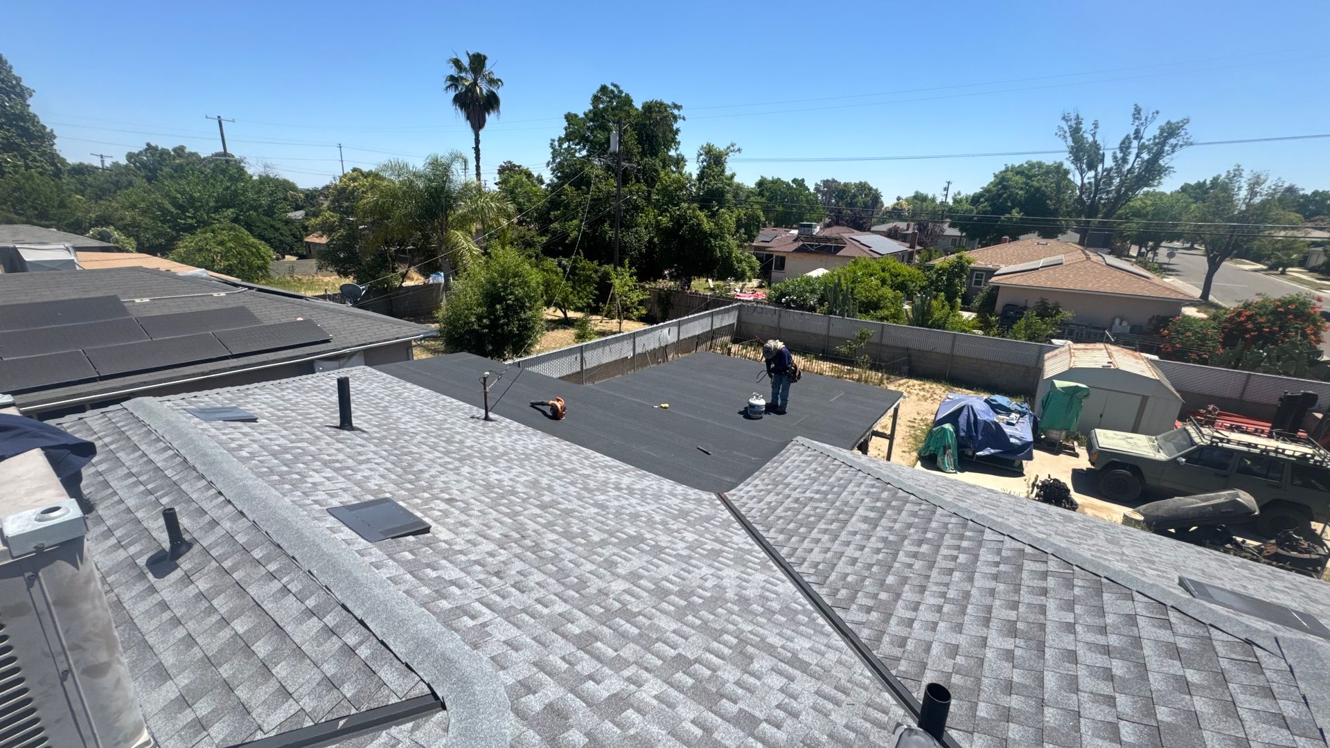 Rooftops in a sunny suburban neighborhood with trees and parked vehicles in the background.