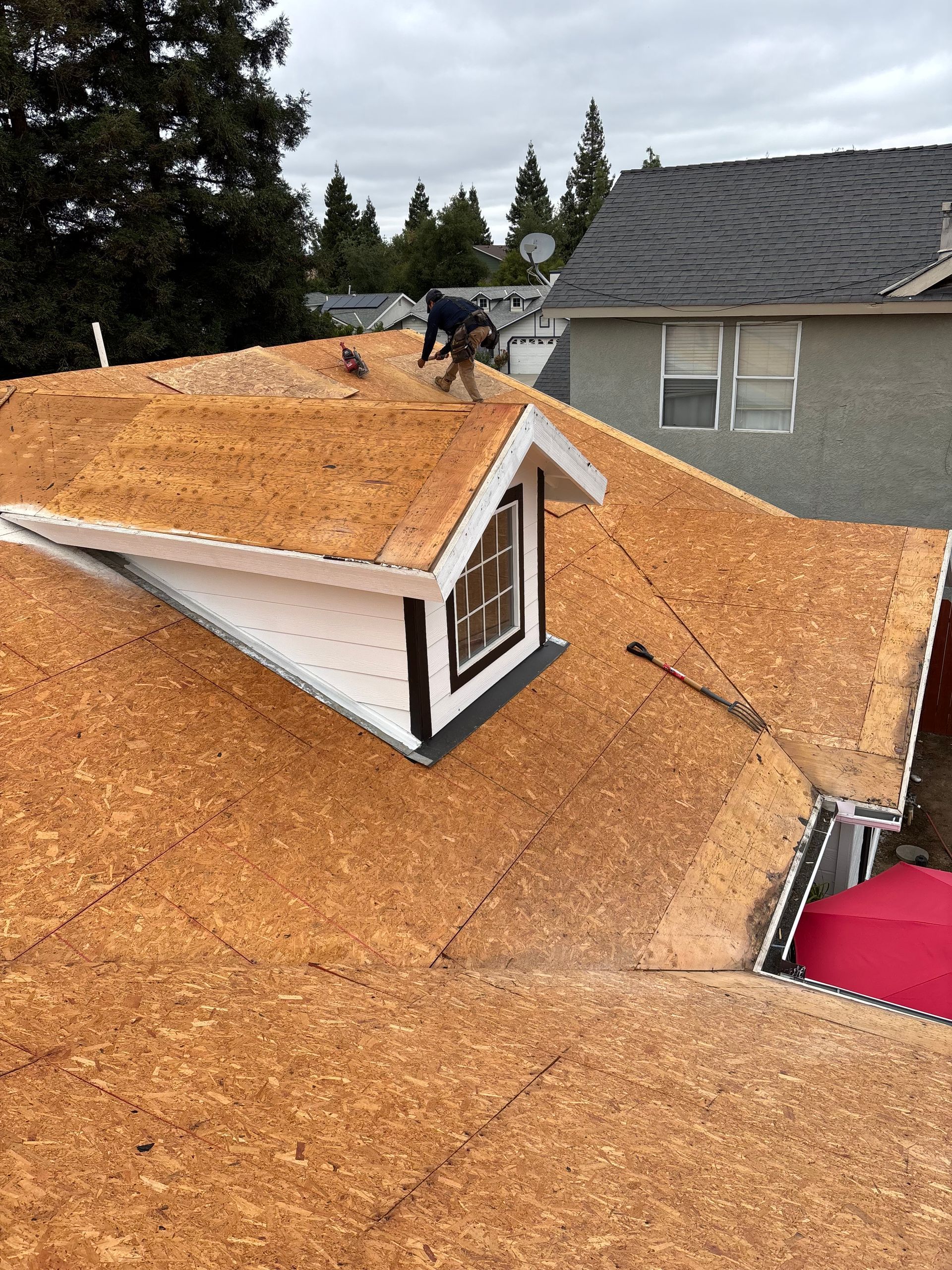 Roof under construction with orange underlayment, dormer window, and worker on the ridge