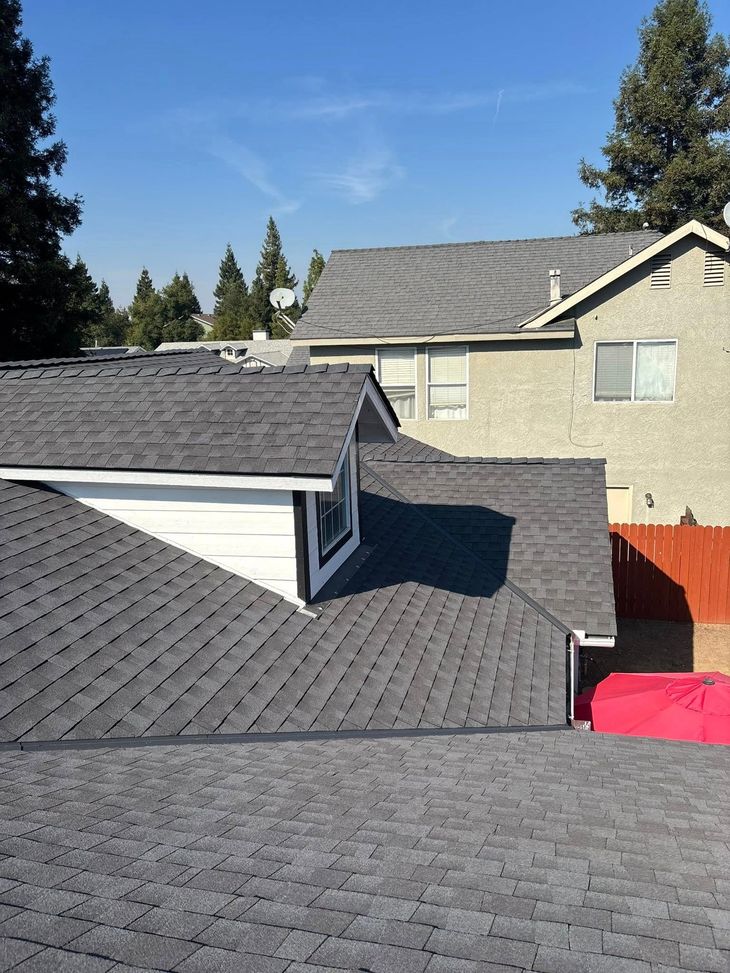 Residential rooftops with gray shingles and beige houses under a clear blue sky
