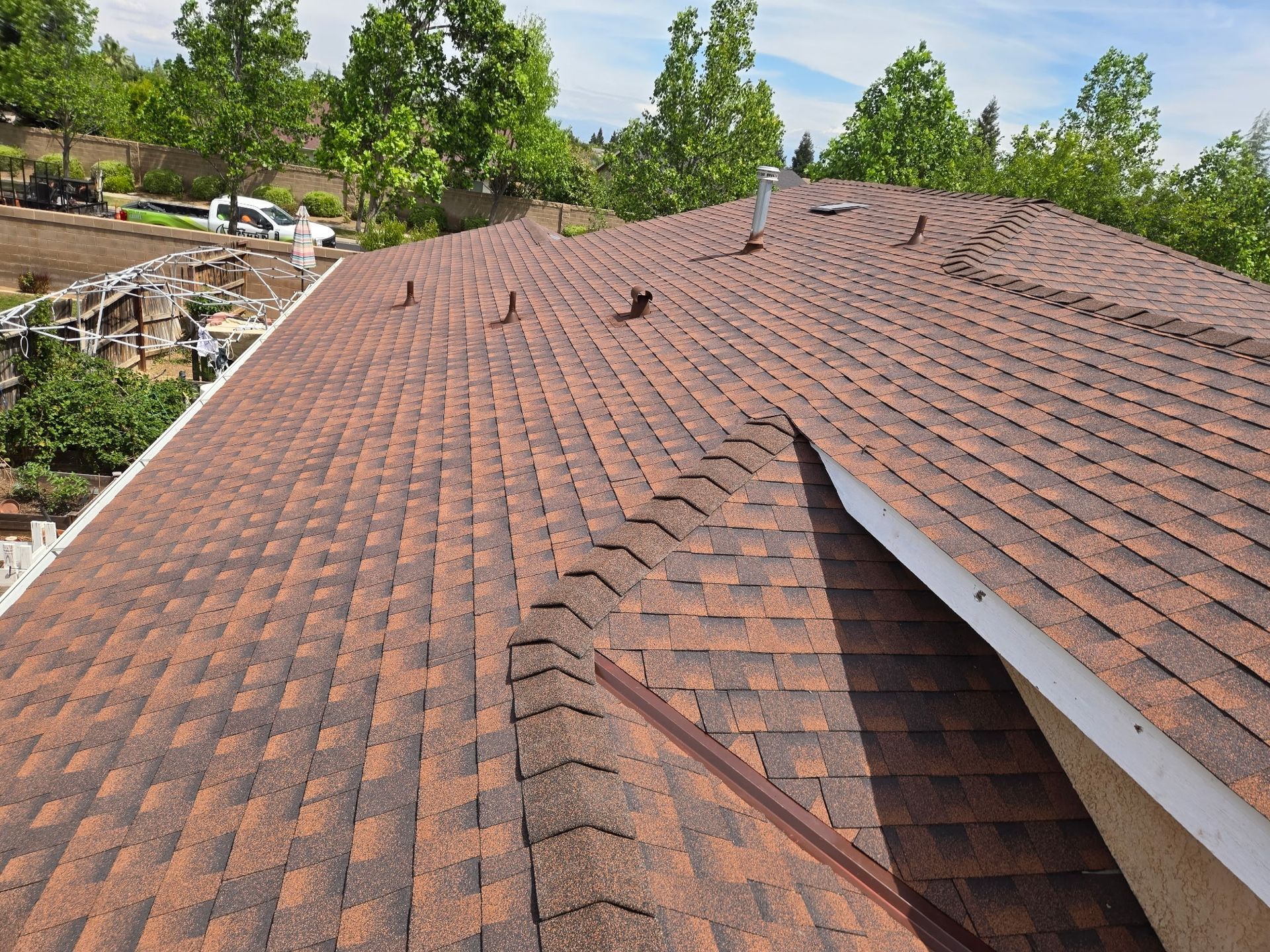 Shingled residential roof with a roof vent and surrounding trees on a sunny day