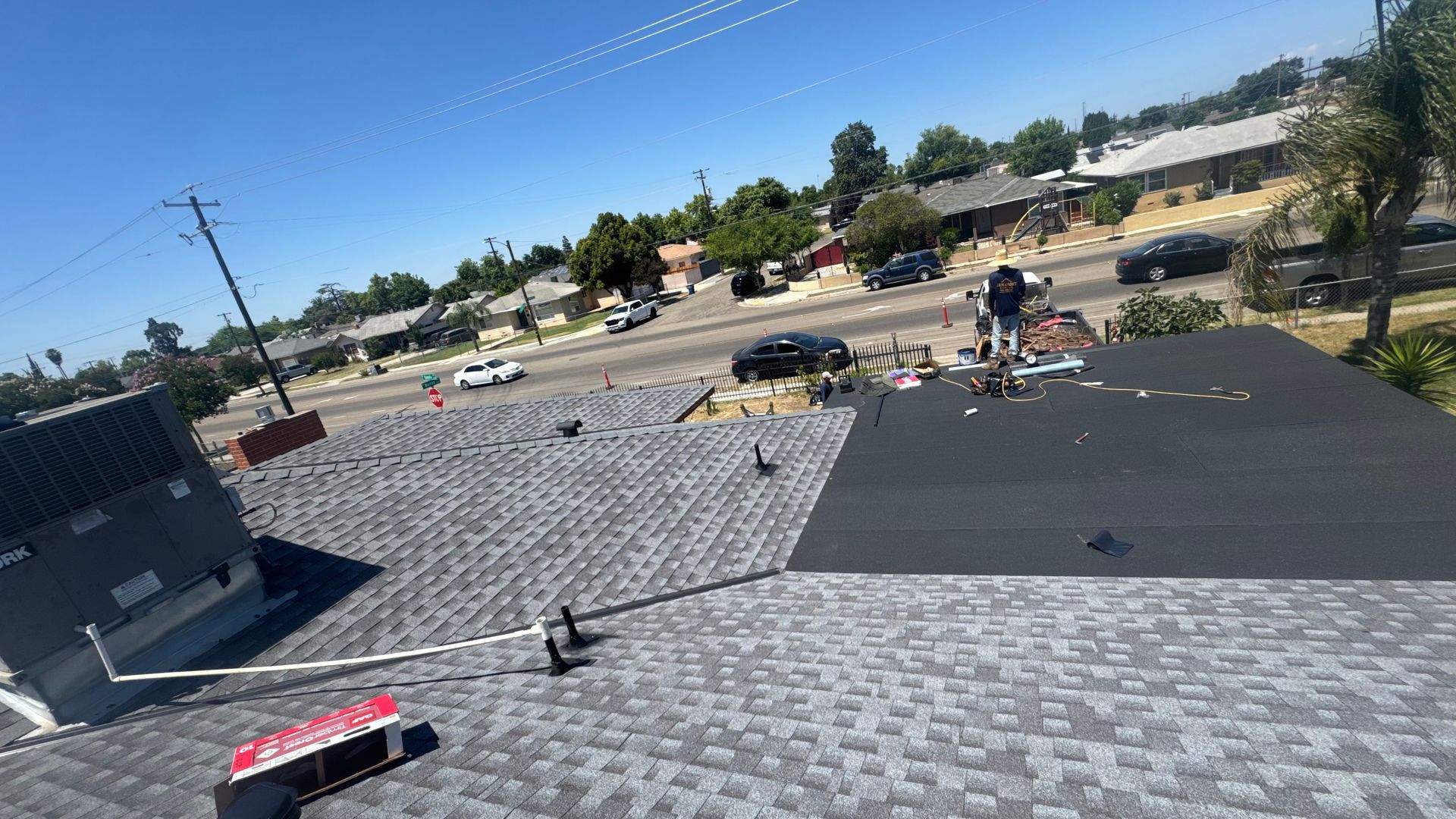 Roof under construction with gray shingles, workers, tools, and a partly finished black roof section.