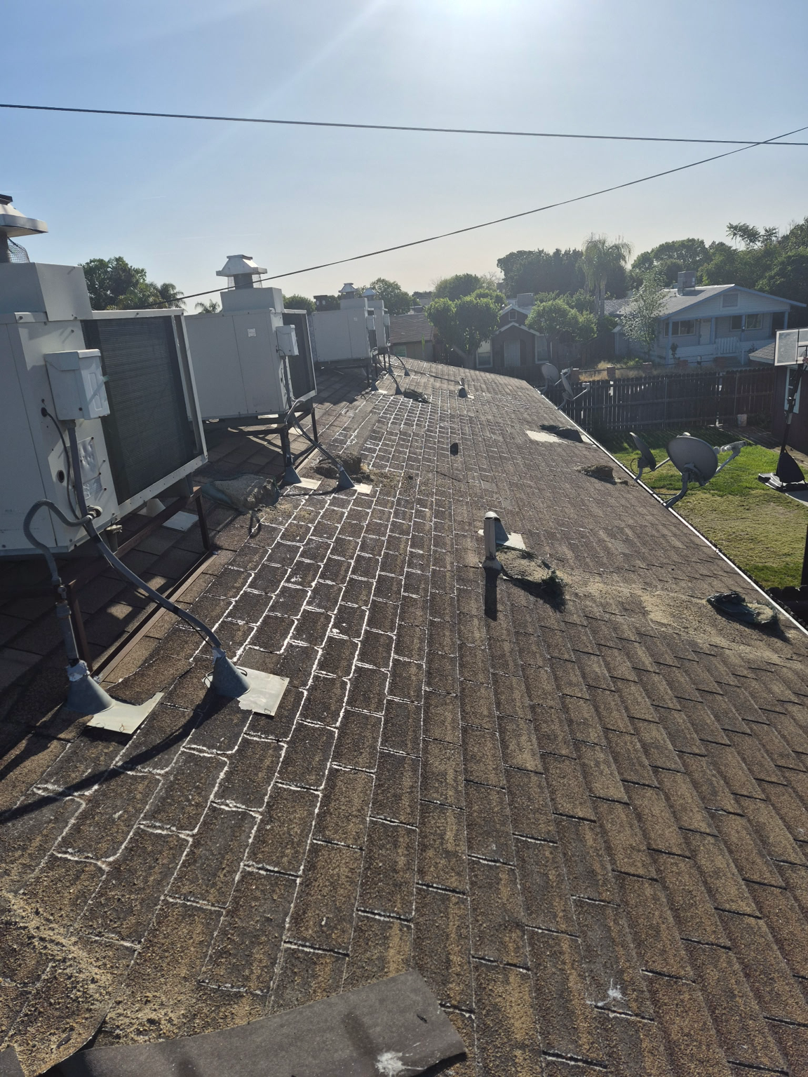Rooftop with gravel shingles, vents, and utility units under a clear sky.