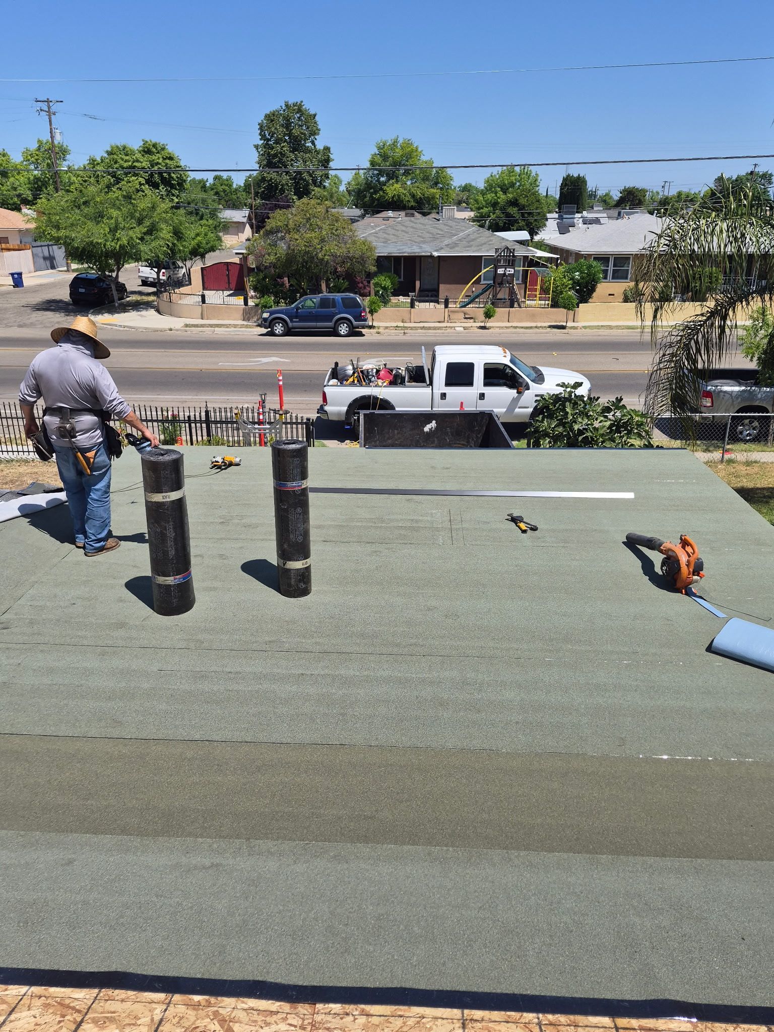 Roof view of a street with a white pickup, a worker, and tools on a sunny day