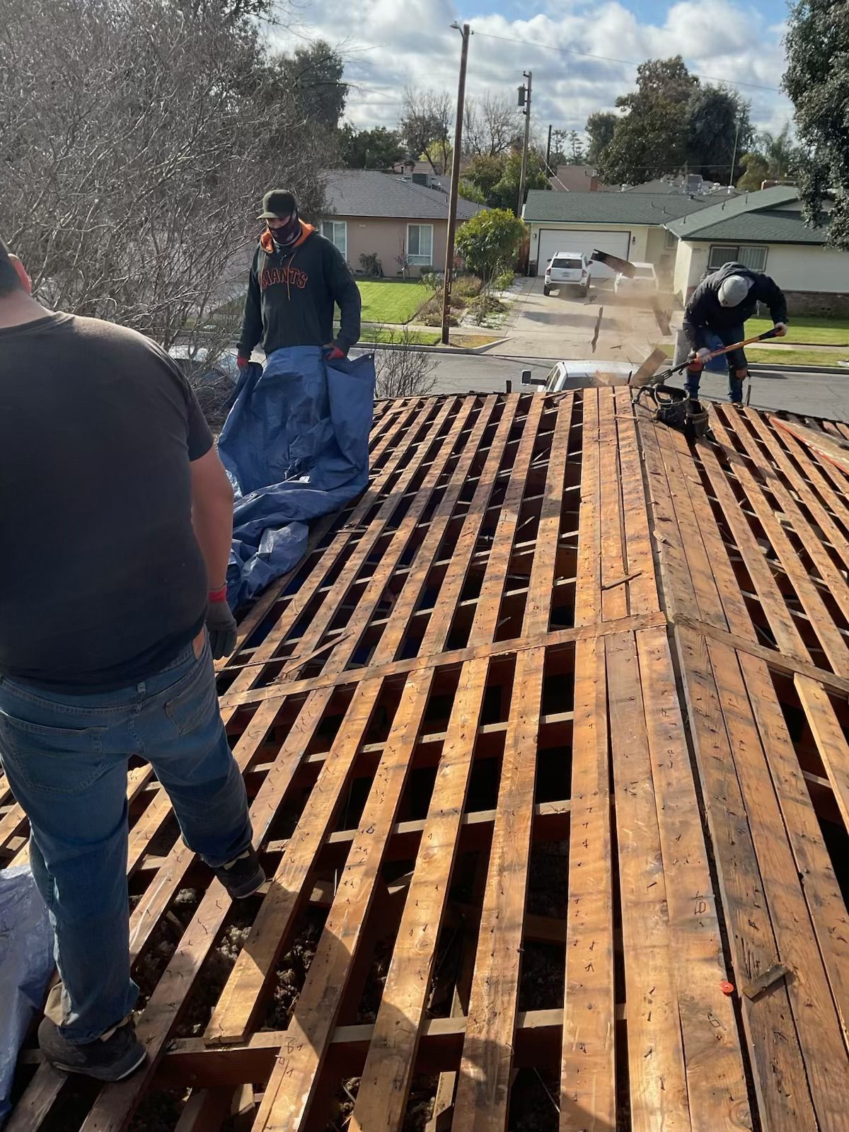 Workers repairing a roof deck with exposed wooden beams on a sunny residential street