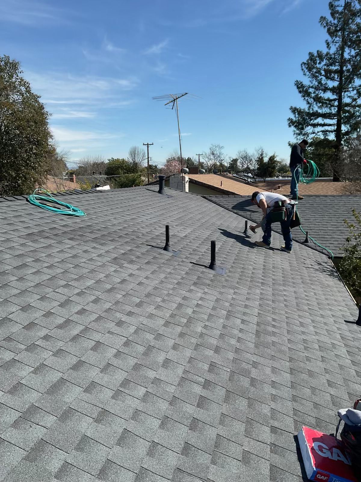 Roof under construction with workers on a gray shingled surface under a clear sky