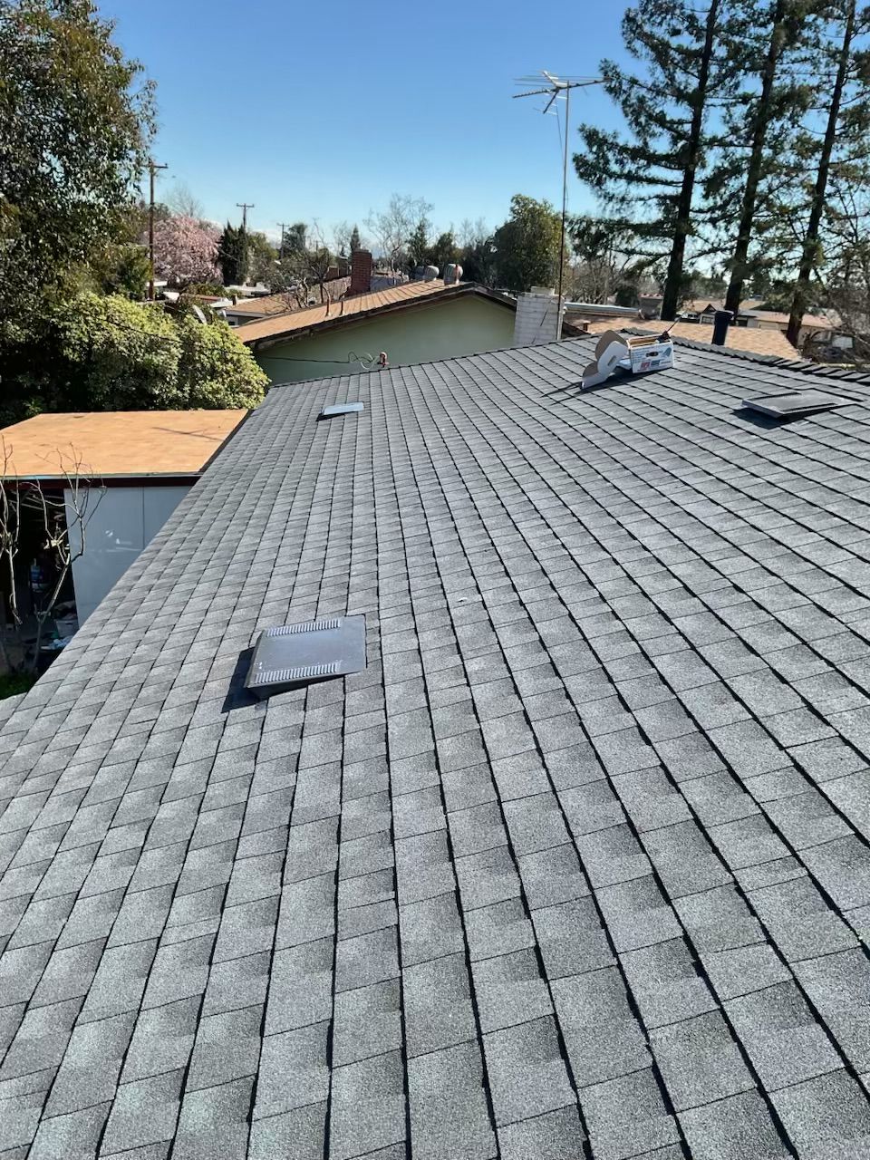 Gray shingle roof with vent covers, trees and a neighboring house in the background
