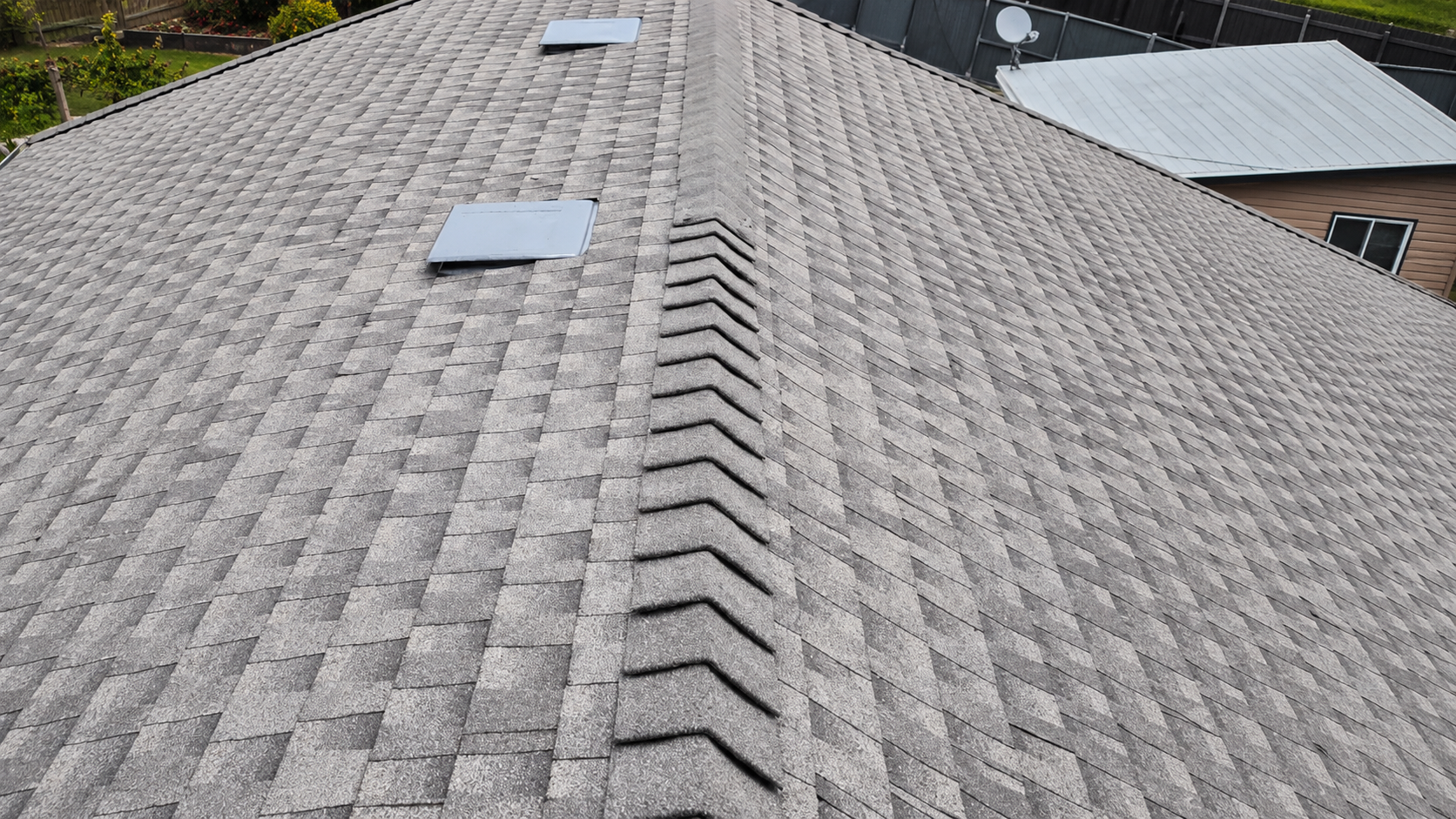 Rooftop view of a residential neighborhood with shingles, chimneys, trees, and blue sky.