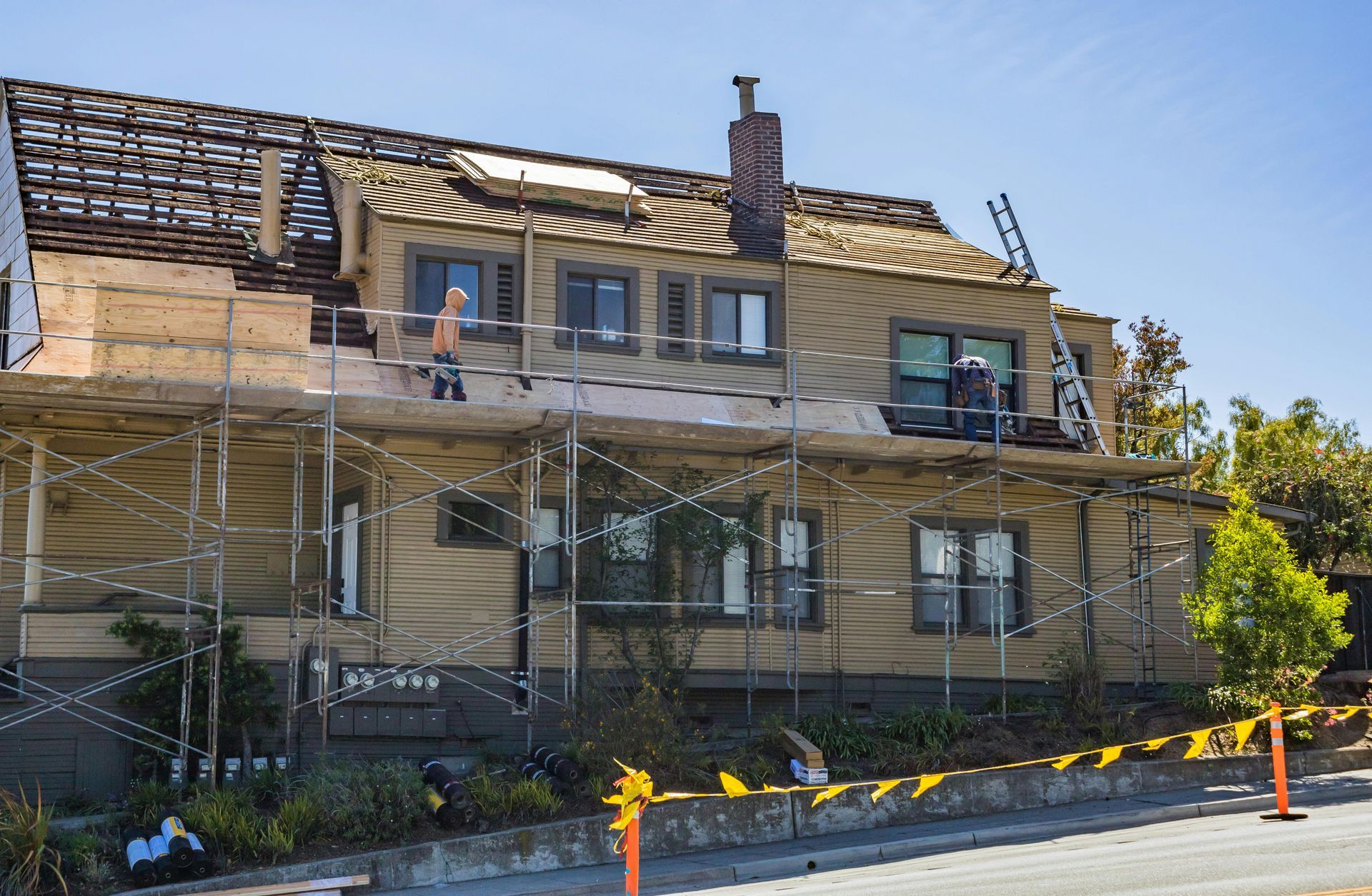 Two-story house under renovation with scaffolding, exposed roof, and workers on the front facade