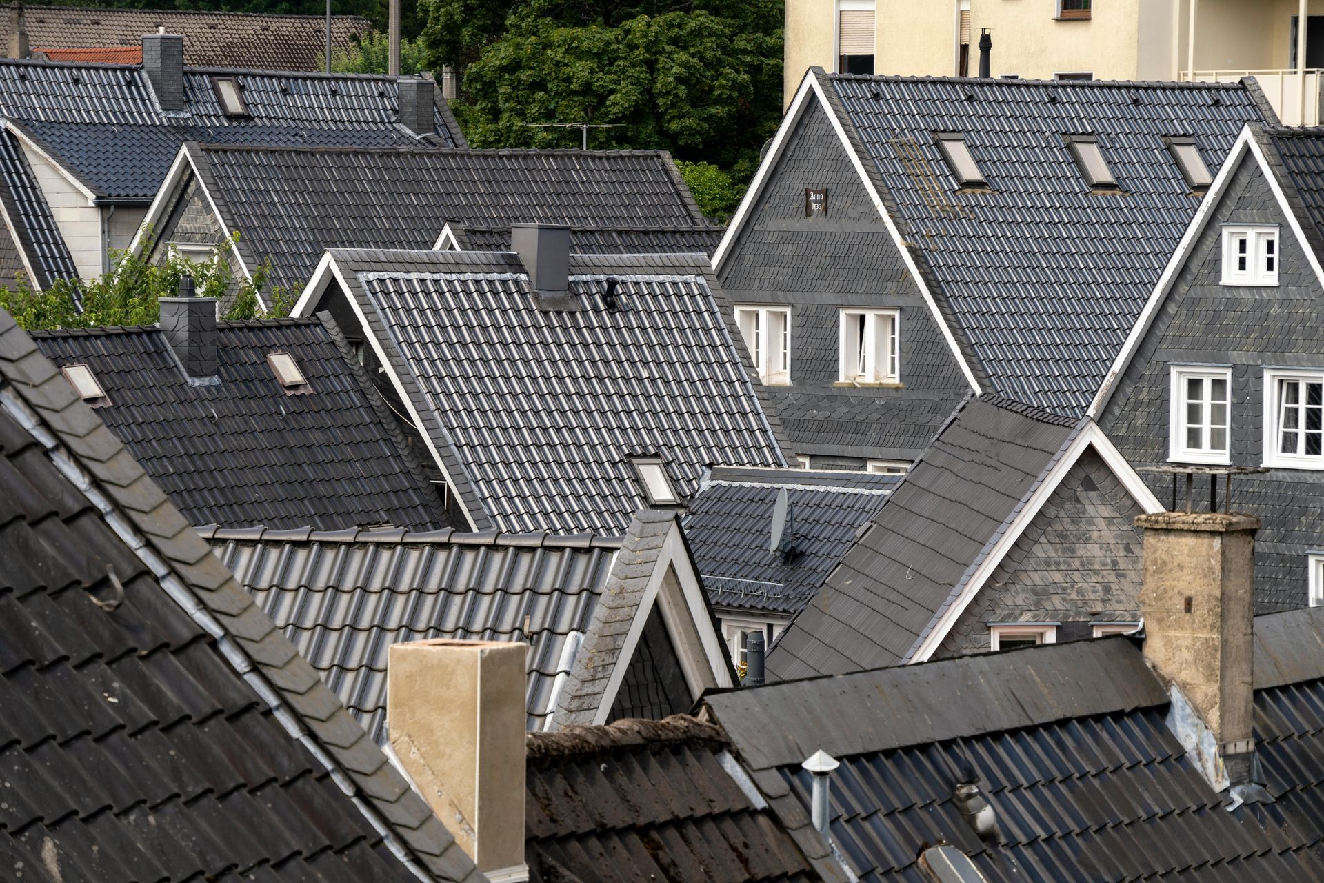 Rooftops with gray slate tiles and several chimneys in a dense residential neighborhood