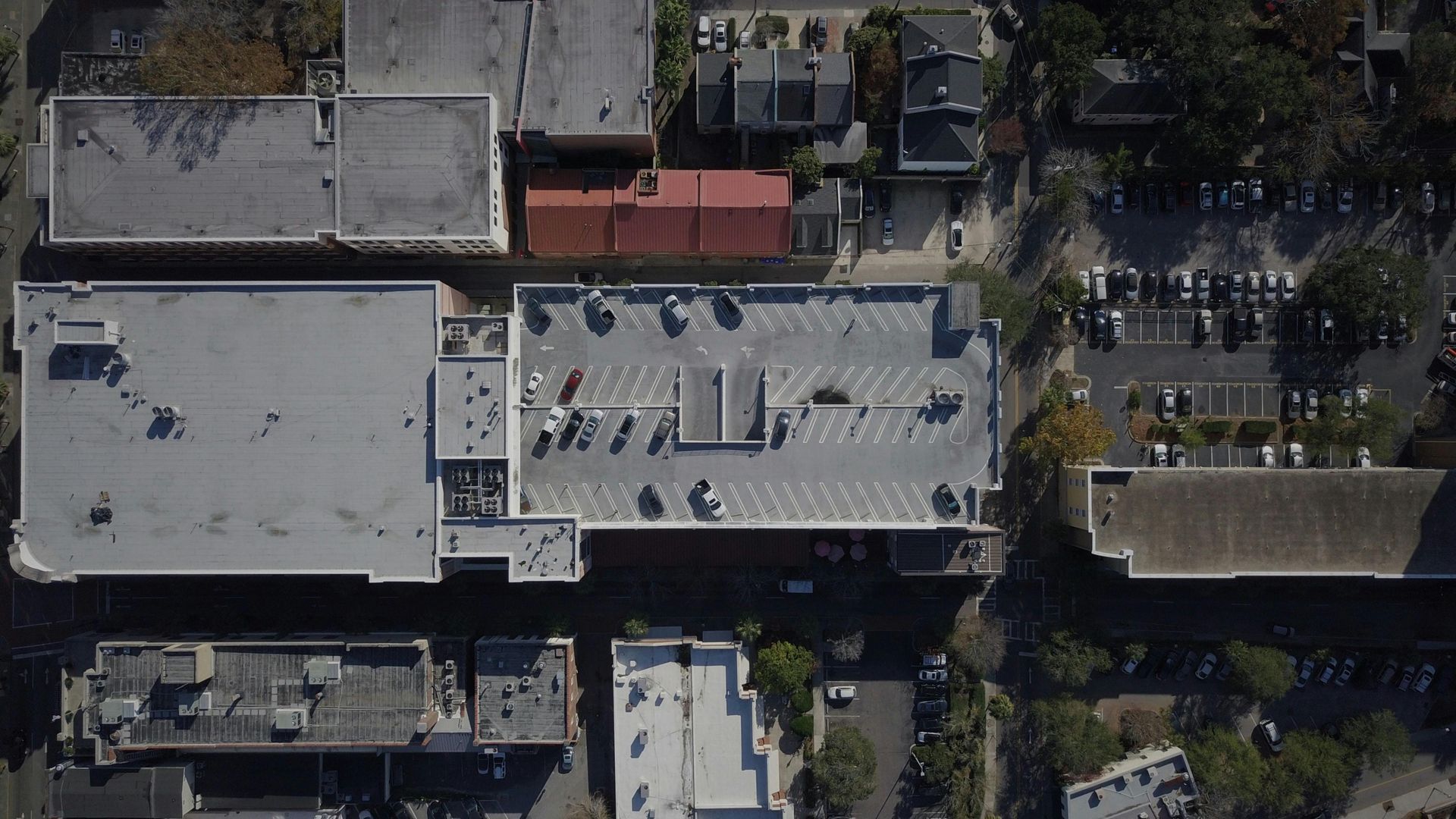 Aerial view of city buildings, rooftops, parked cars, and tree-lined streets.