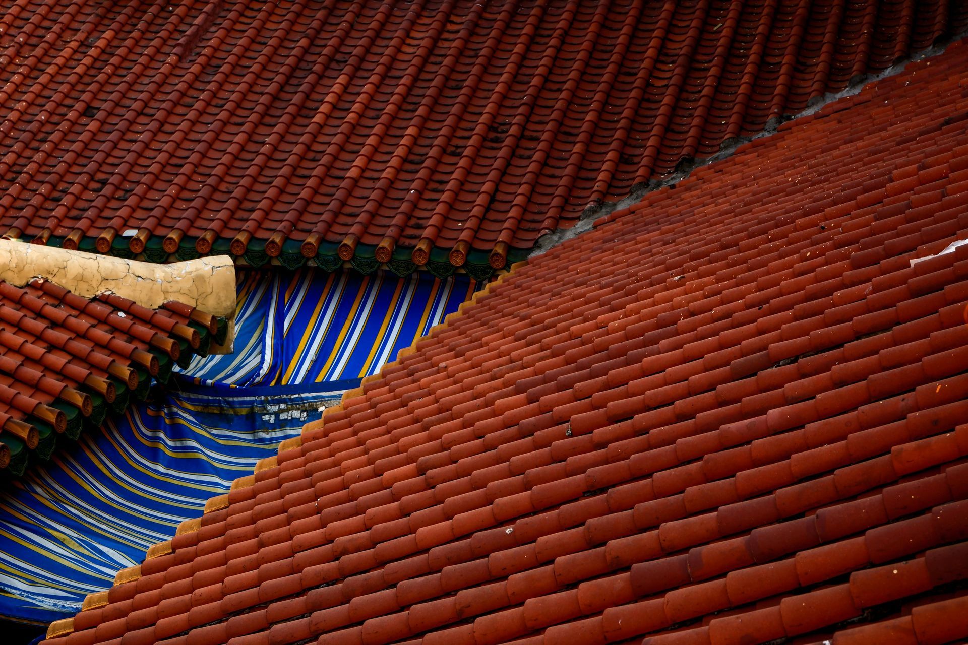 Red-tiled rooftops with blue tarps between sloping roof sections