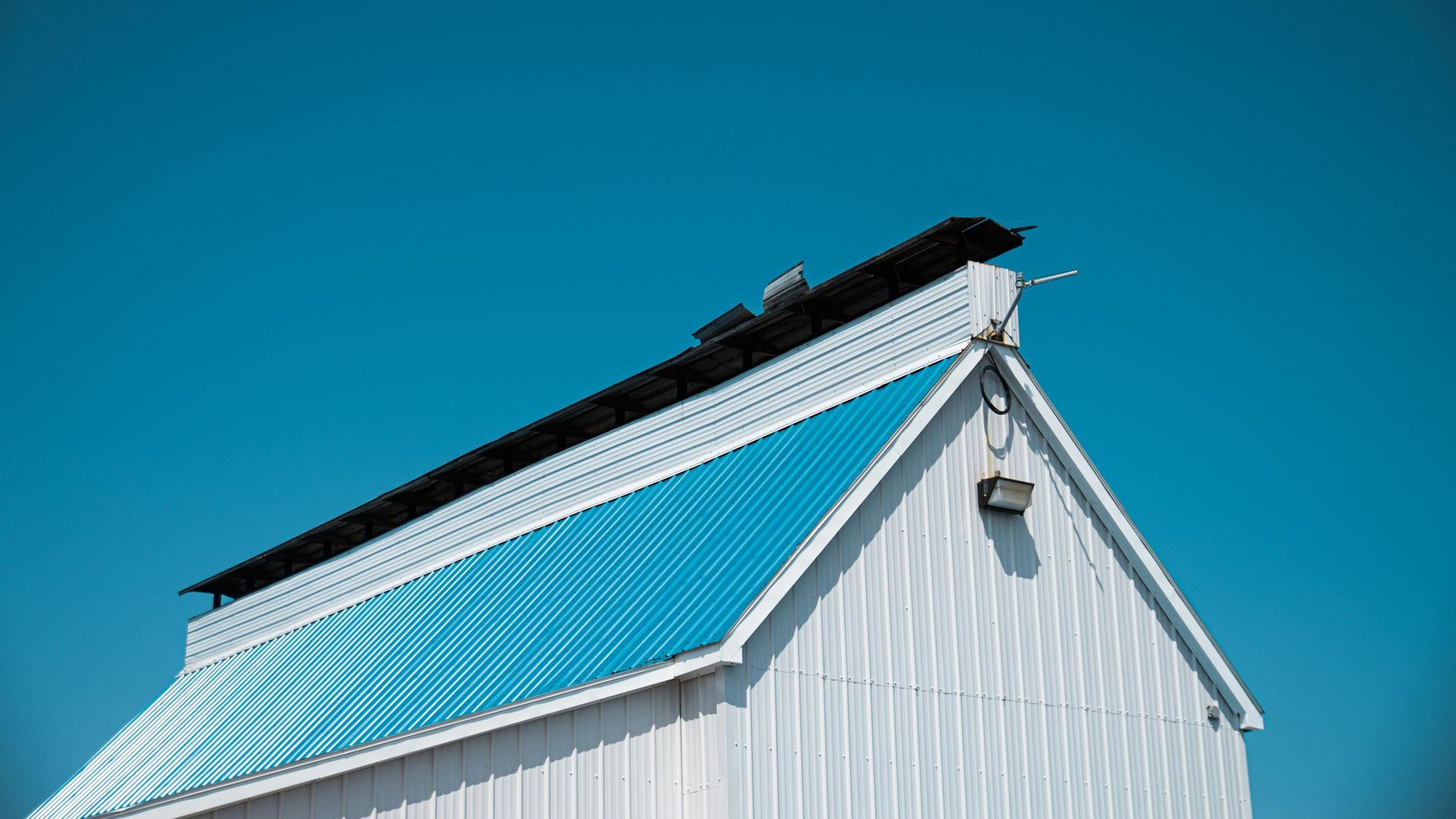 White house gable roof with bright blue metal panel against a clear blue sky