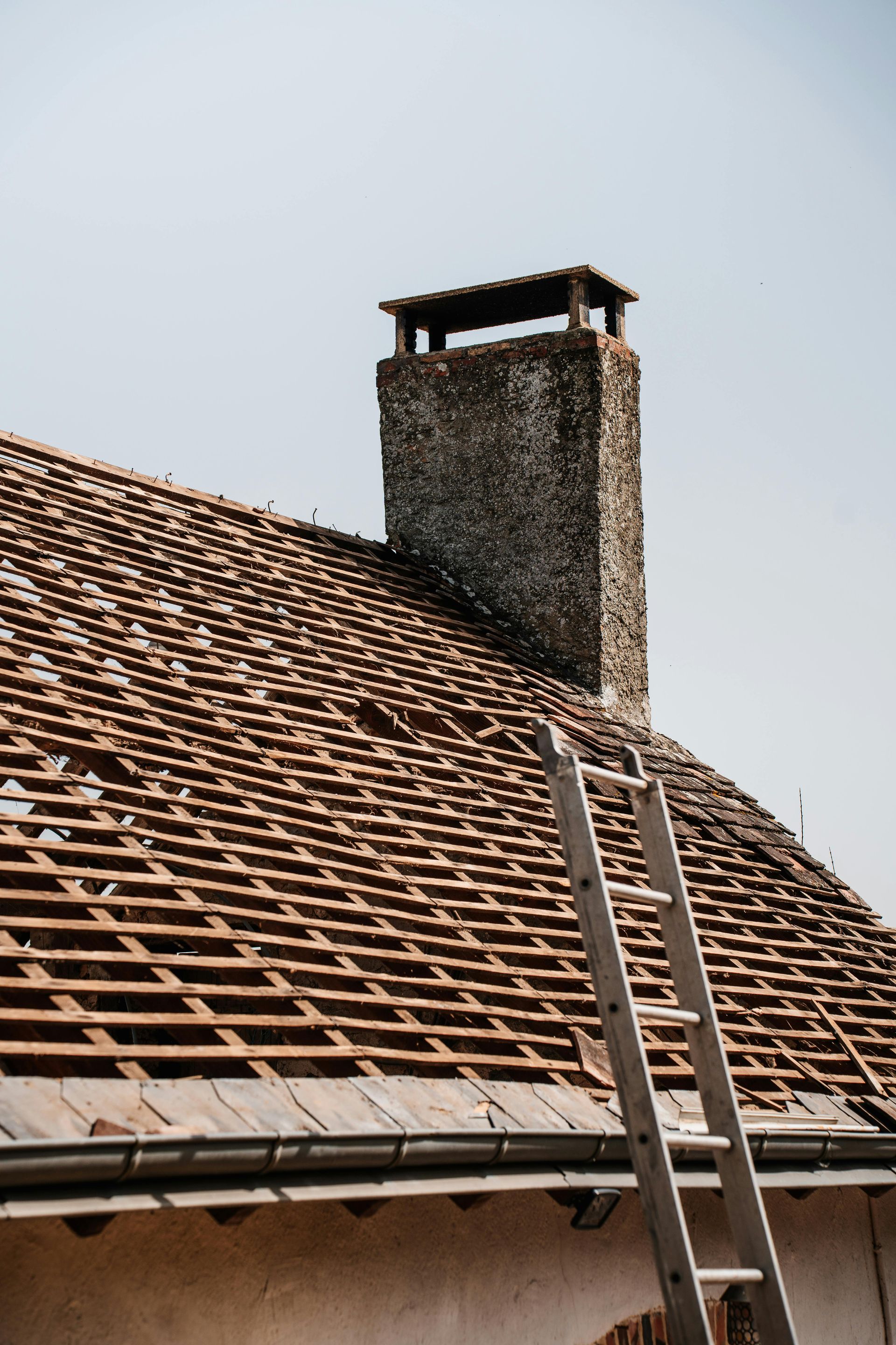 Rooftop with weathered brown tiles and a stone chimney against a pale sky