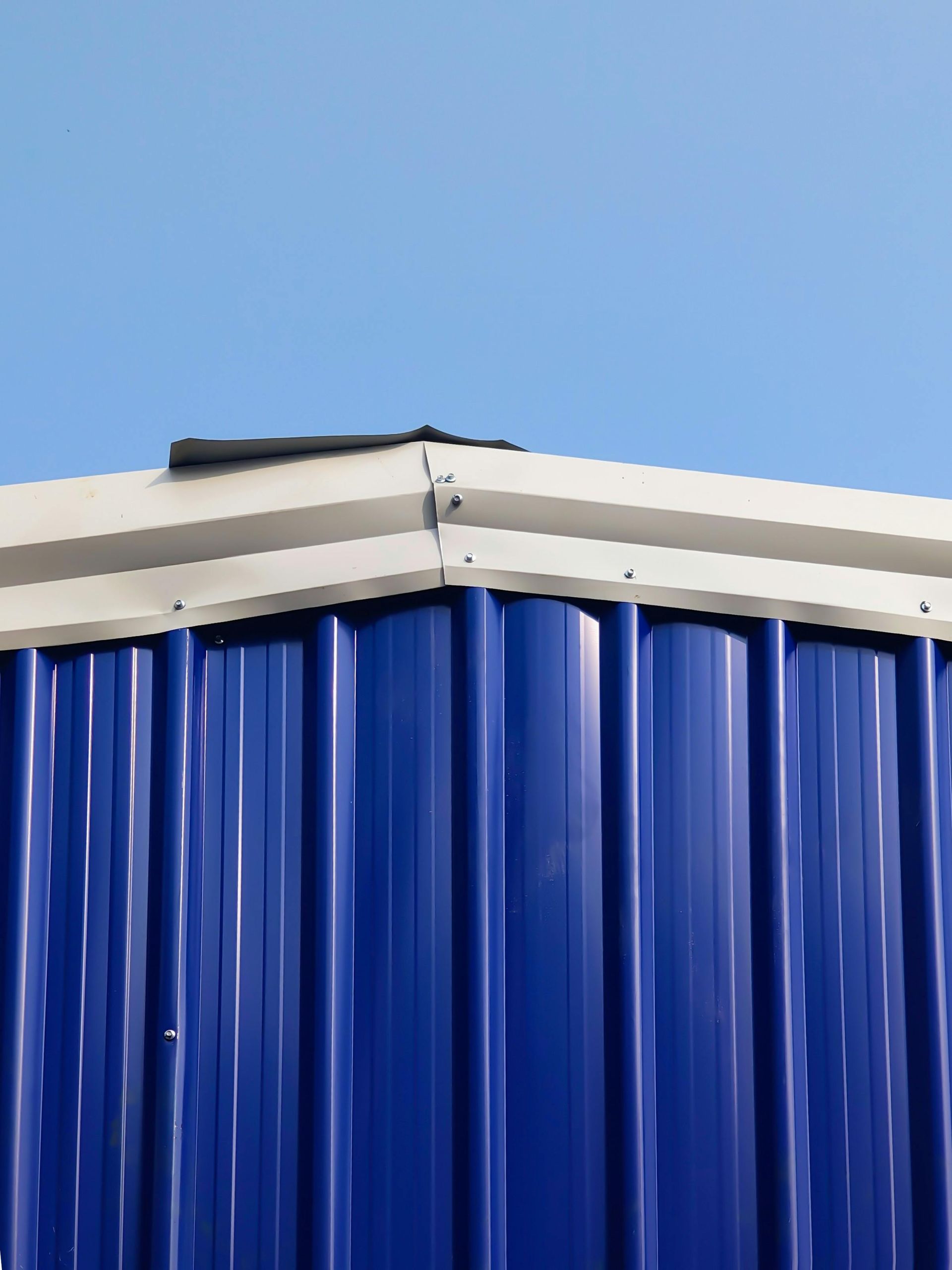 Blue corrugated metal wall beneath a white roof against a clear sky