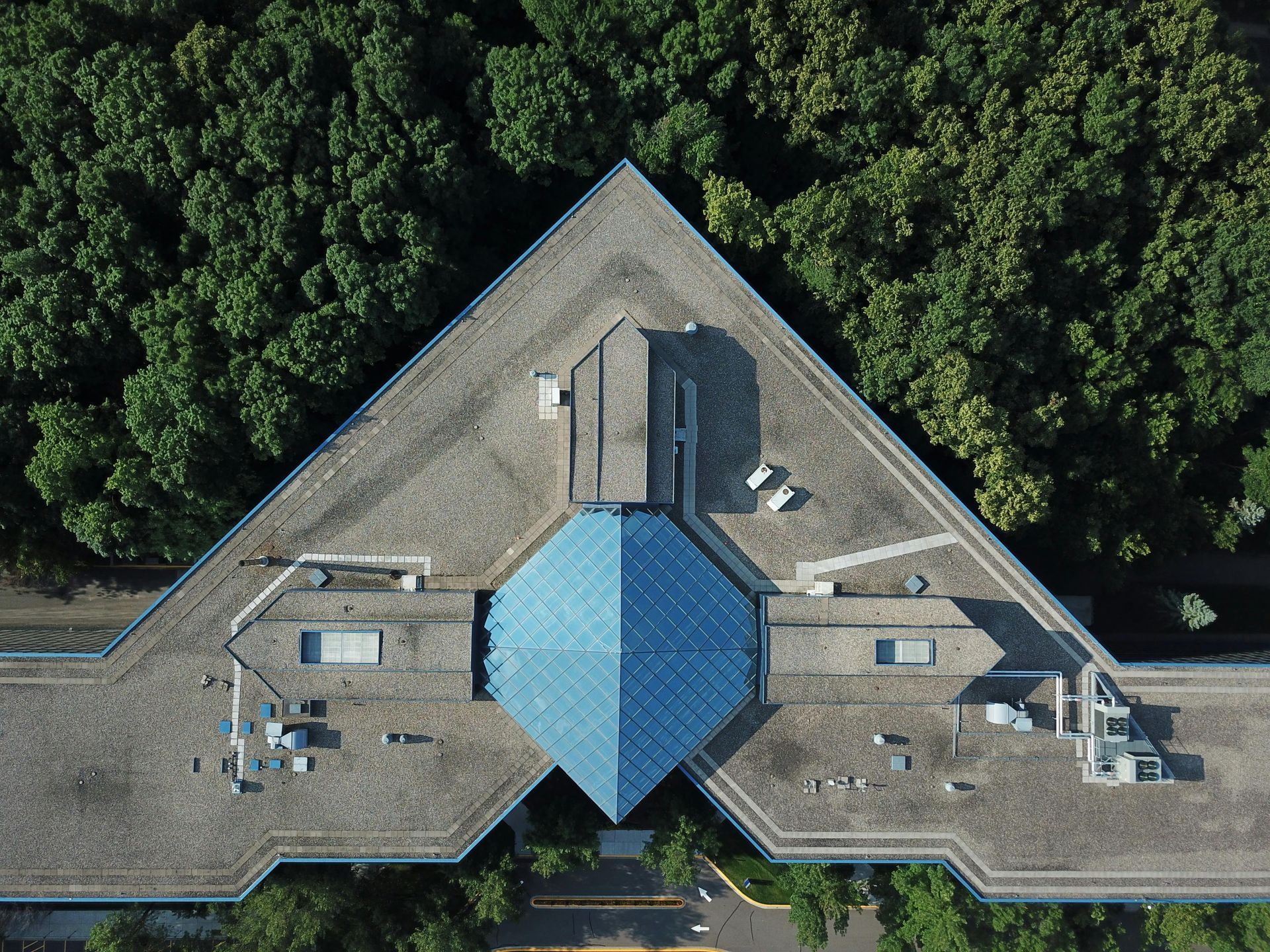 Aerial view of a large building with a blue roof, surrounded by dense green trees.