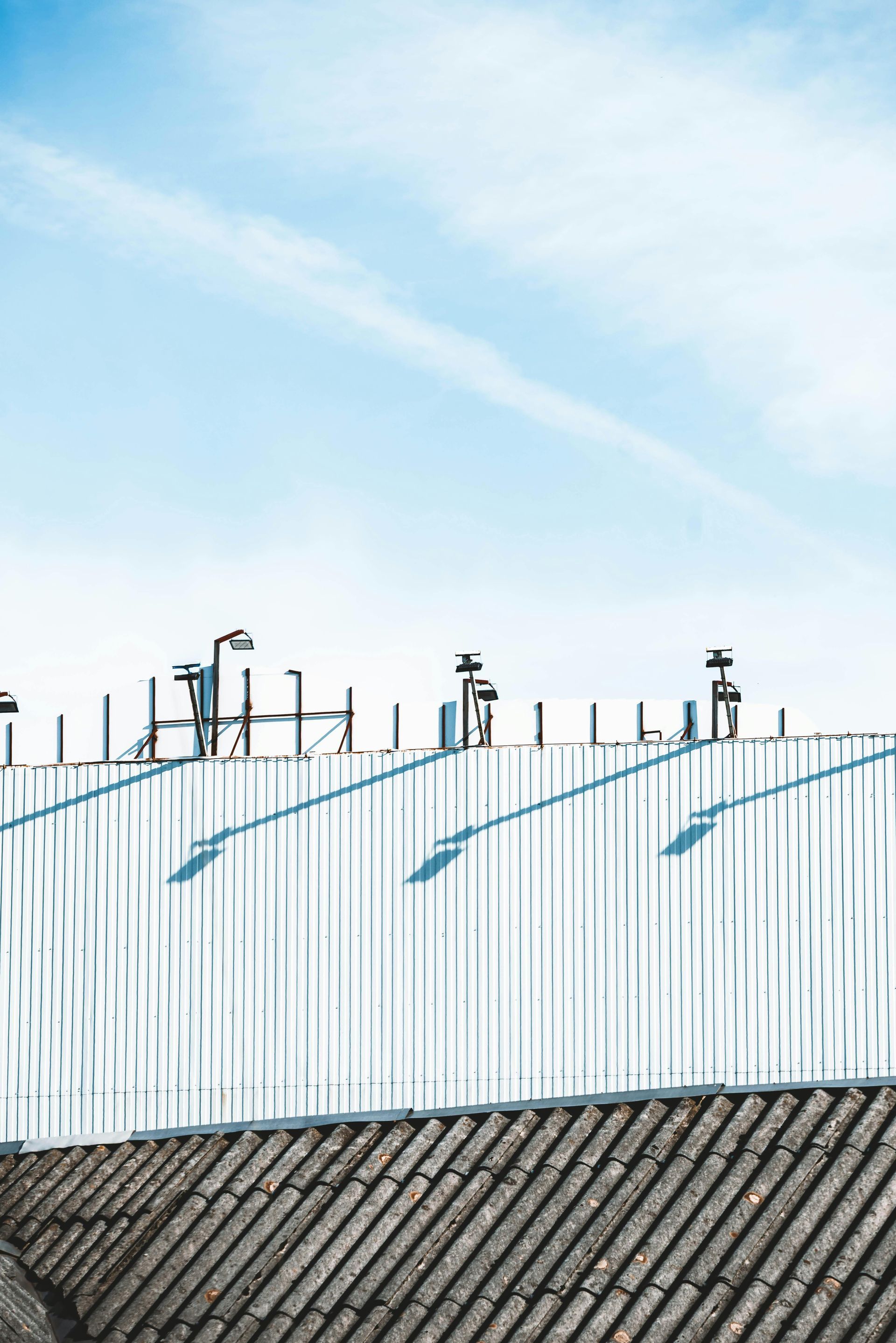 Tall corrugated metal fence with pipes above a sloped roof under a clear blue sky