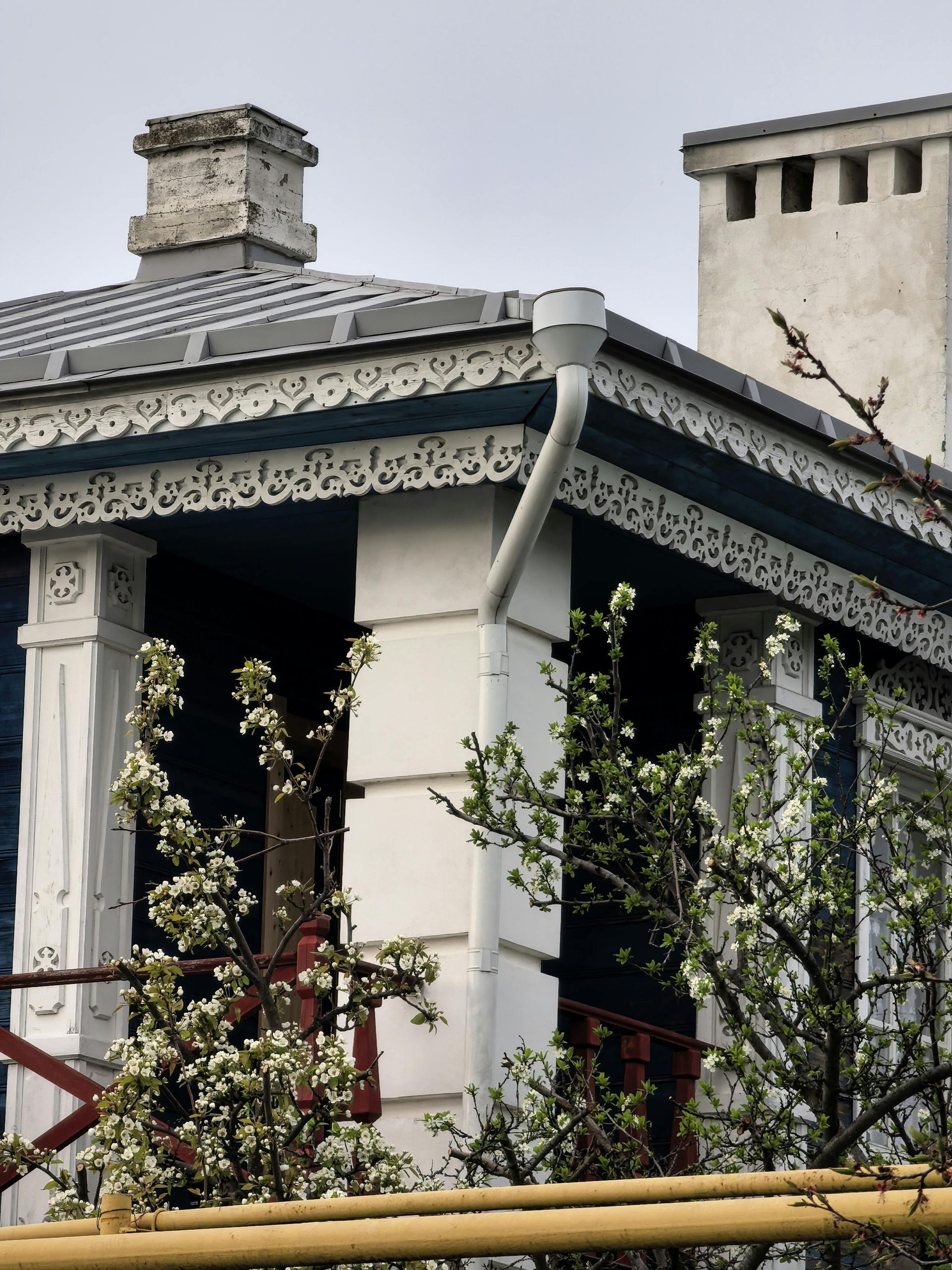 Victorian-style house porch with white columns, dark trim, and climbing greenery against a stone wall.