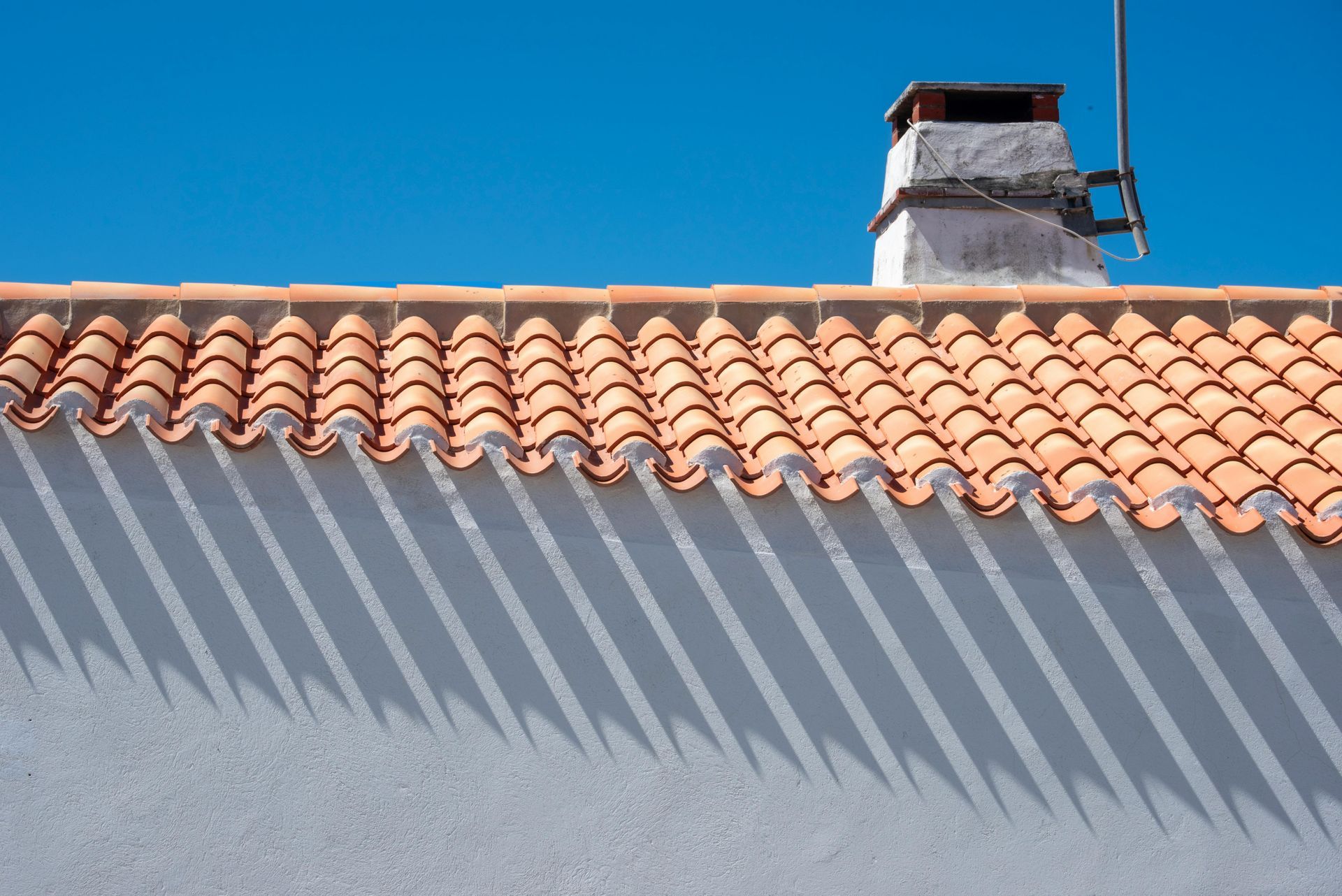 Terracotta-tiled rooftop with a chimney against a bright blue sky