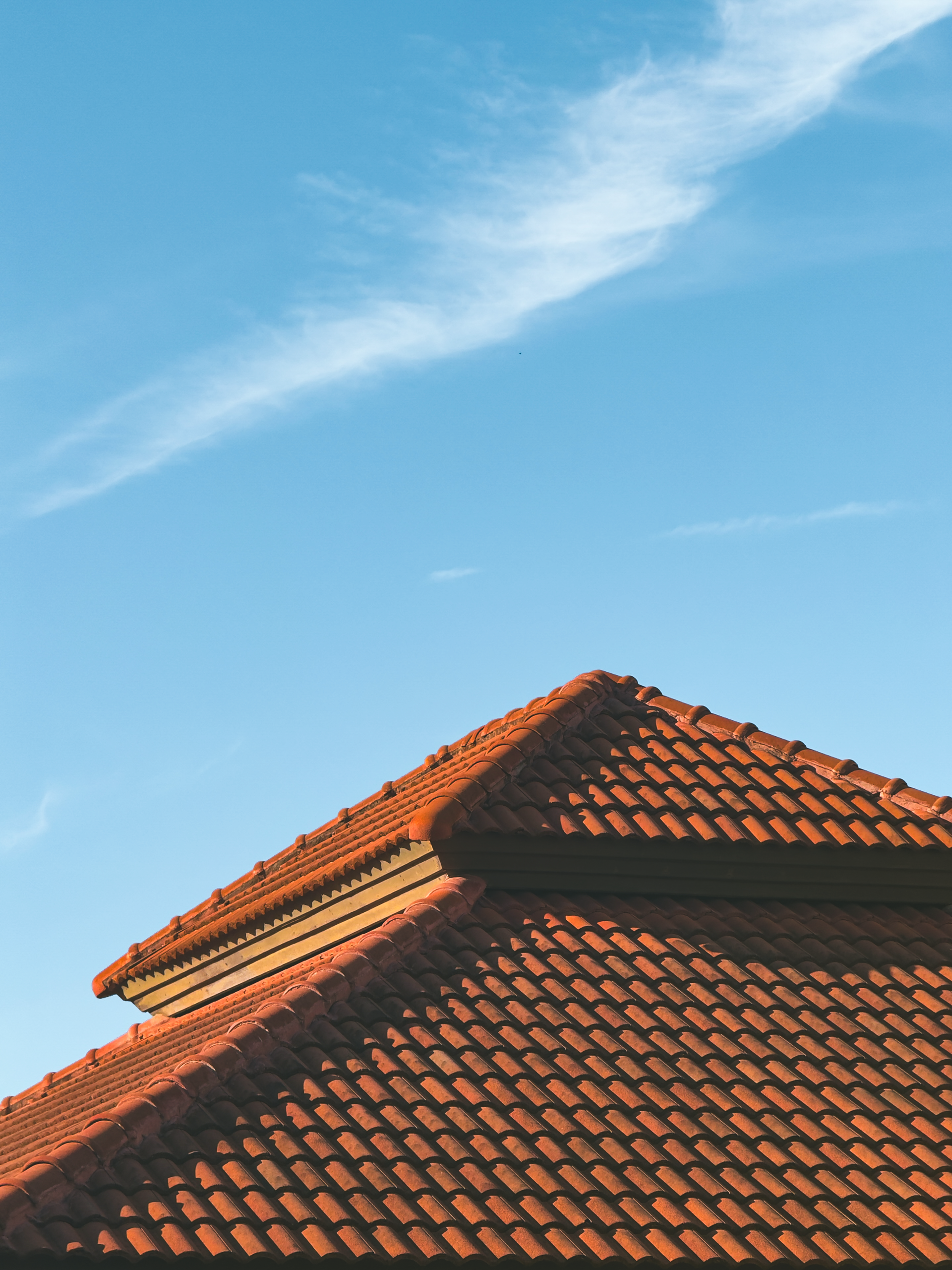 Red tiled roof against a clear blue sky with wispy clouds