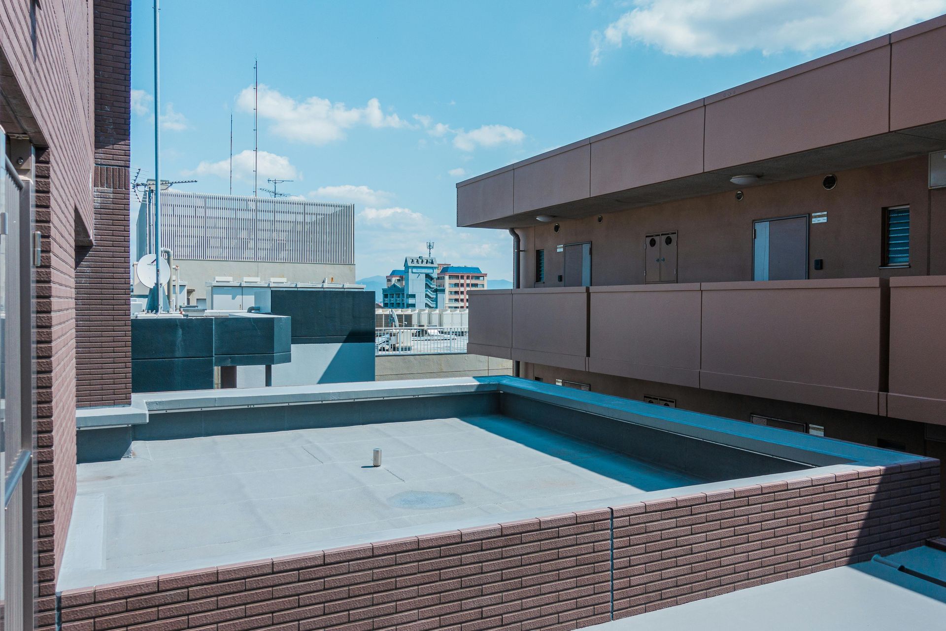 Rooftop terrace with a small pool, brick walls, and city buildings under a blue sky