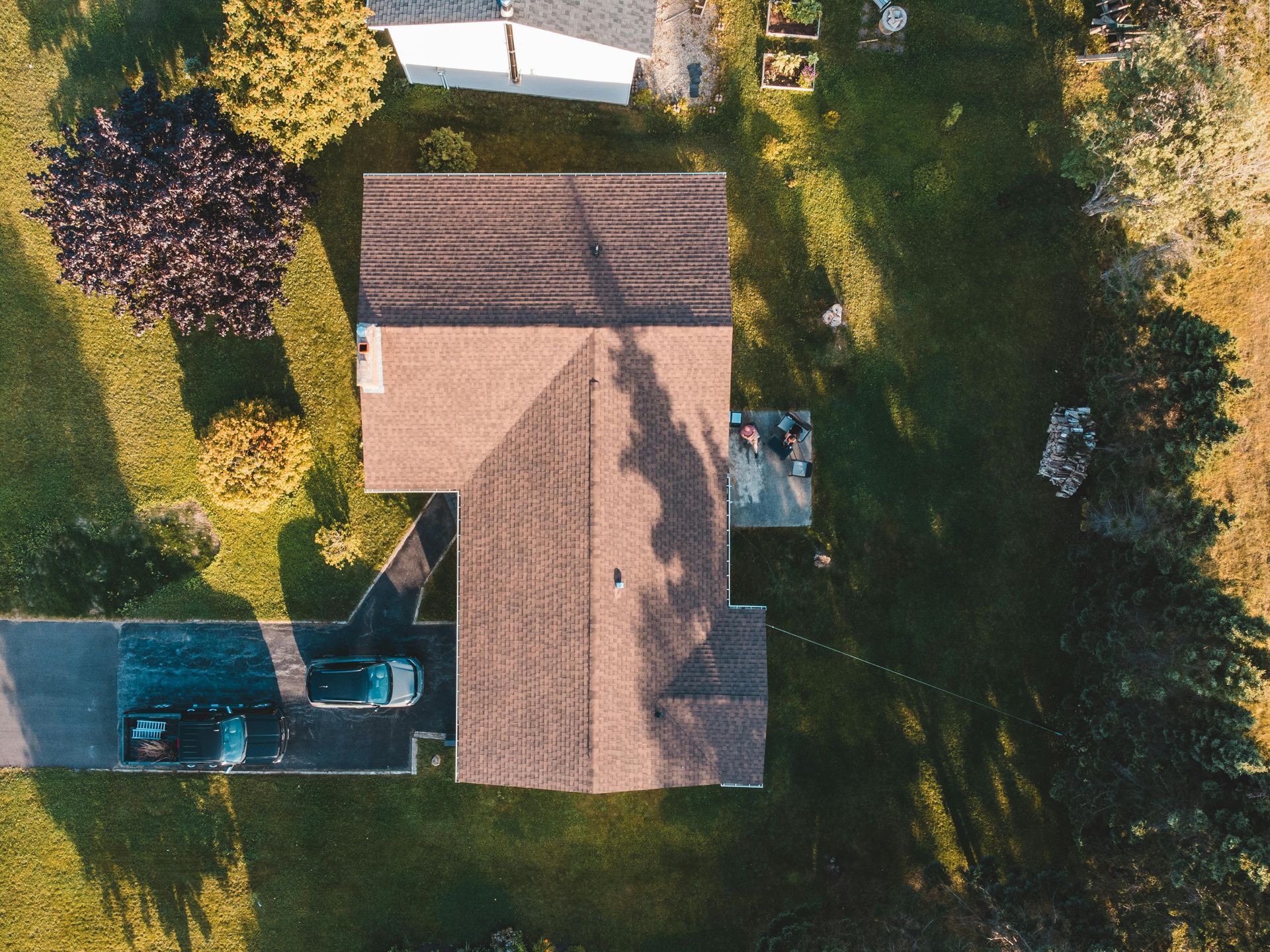 Aerial view of a house with a brown roof, backyard trees, and a parked truck beside it.