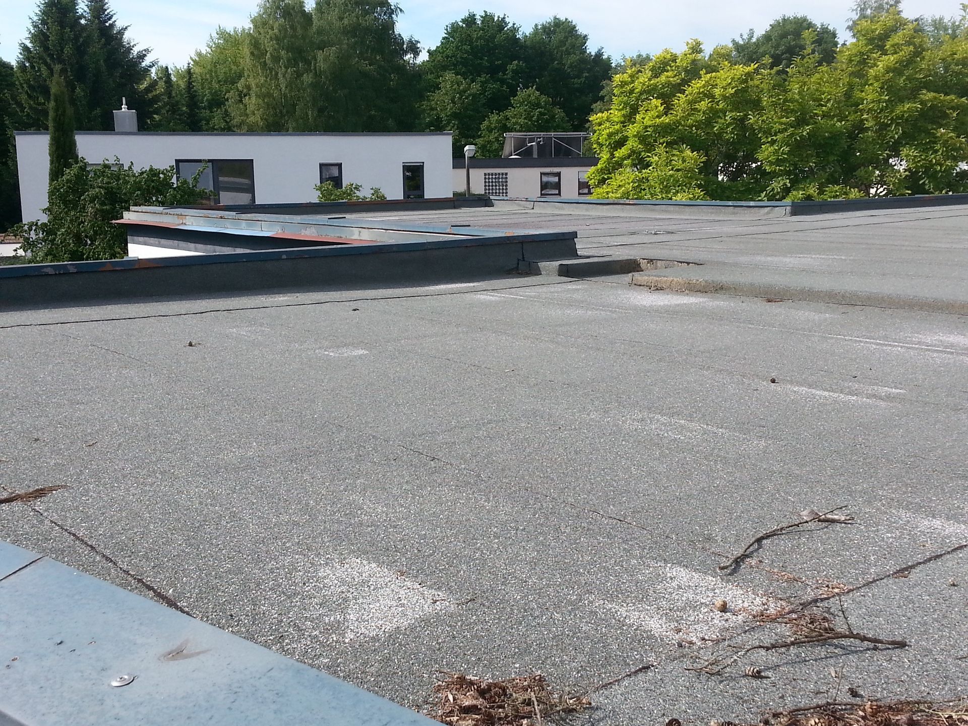 Flat rooftop with gravel, low white buildings, and trees in the background under a clear sky