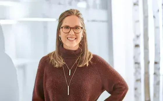 Eine Frau mit Brille und Pullover lächelt in die Kamera.