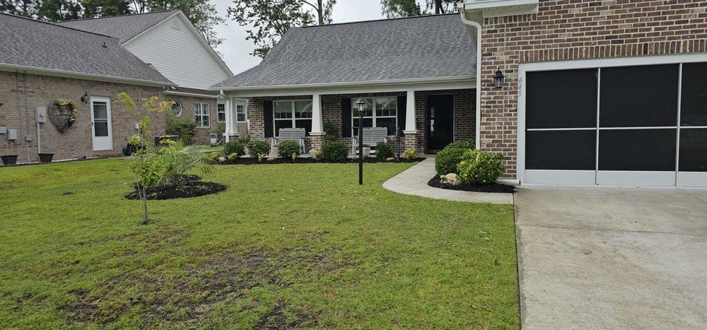 A tan brick house with a gray roof and a screened-in garage, featuring a front porch and a green grassy lawn.