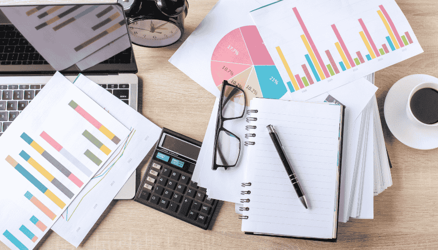Desk with charts, calculator, notebook, glasses, pen, and coffee, showing a business workspace with analytics.
