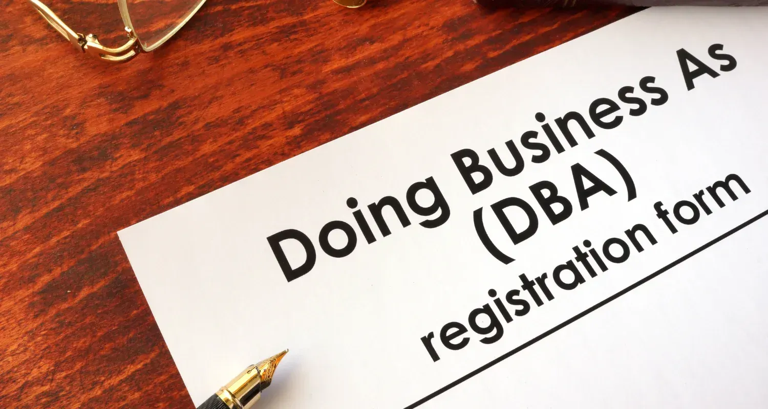 Doing Business As (DBA) registration form on a desk with a pen and glasses nearby