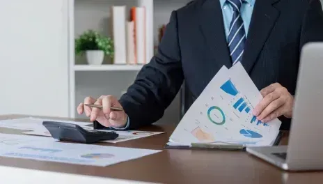 Businessperson reviewing charts at a desk with a calculator and laptop