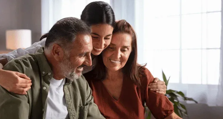Three people smiling and hugging on a couch in a bright living room