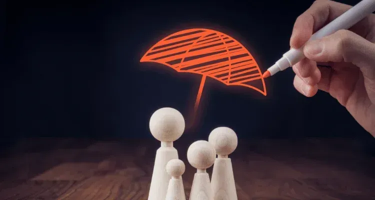 Hand drawing a red umbrella over small wooden figures on a dark table