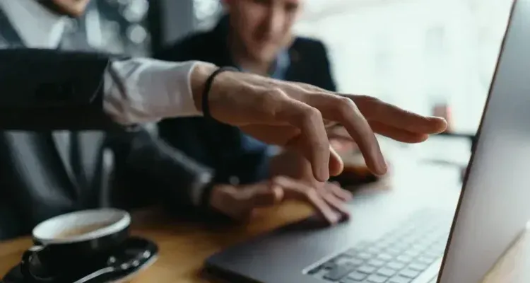 Hands typing on a laptop beside a coffee cup in a blurred office setting