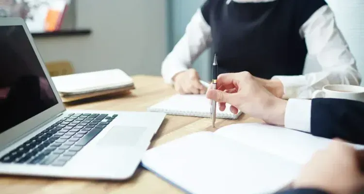 Colleagues discussing documents at a table beside a laptop in a bright office meeting room