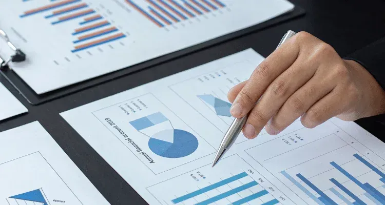 Hand holding a pen over blue business charts and graphs on a desk
