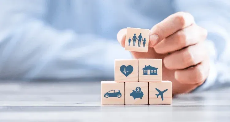 Hand placing a family icon block atop stacked insurance icons on a table