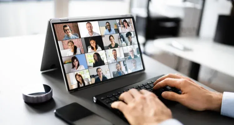Person typing on a laptop during a video conference with multiple participants on screen