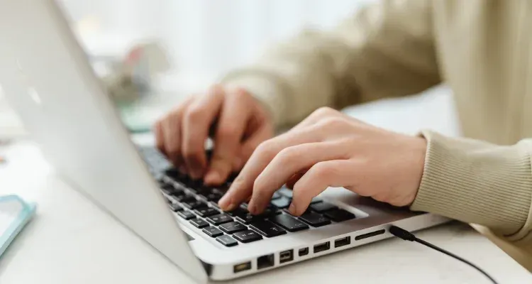 Hands typing on a laptop keyboard beside a smartphone on a desk