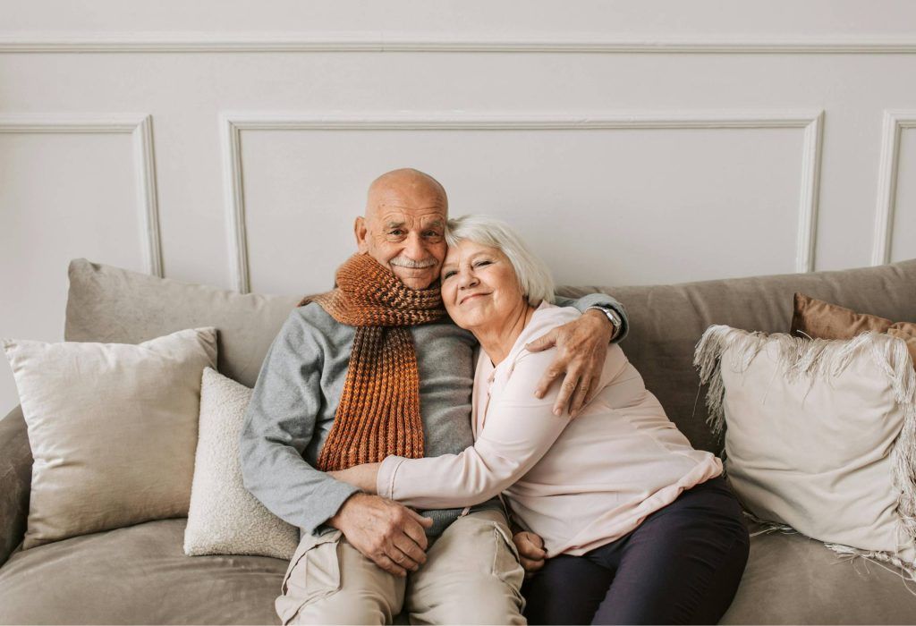 Couple hugging on a gray couch in a bright living room, smiling warmly